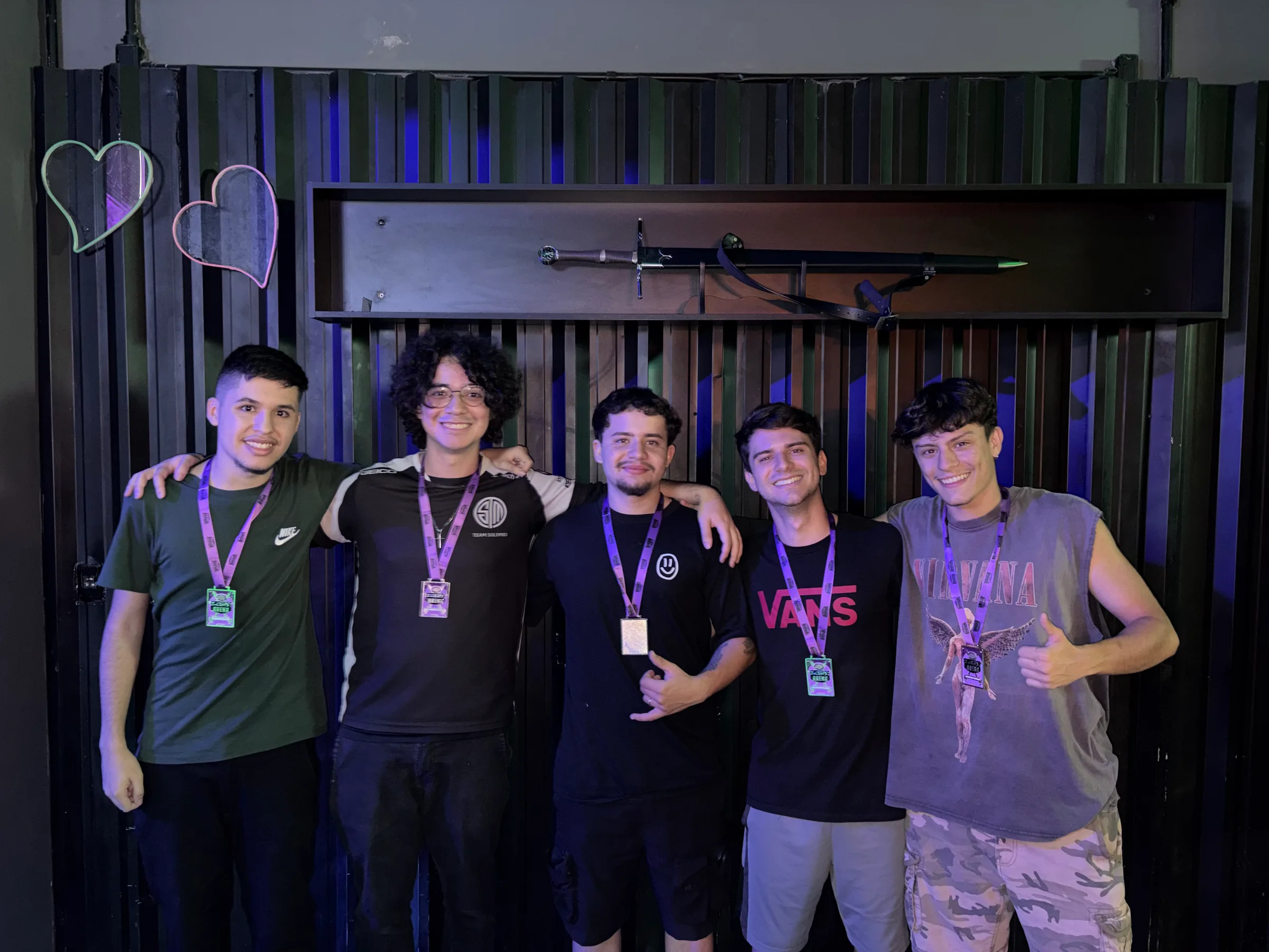 Time Arretados em bastidor descontraído na Login Arena, braços nos ombros e polegares pra cima.
